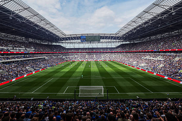 A low-angle, atmospheric shot inside a massive soccer stadium during twilight. The vibrant green grass pitch occupies th